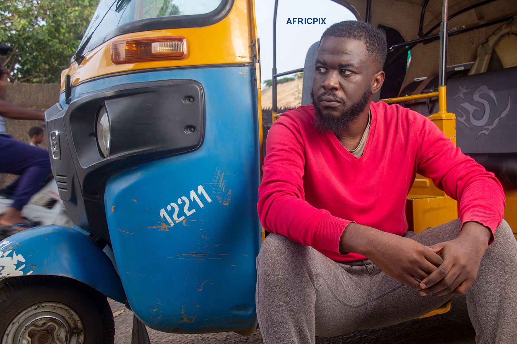 A  African tricycle rider, also known as Keke or Maruwa sitting  behind of his tricycle